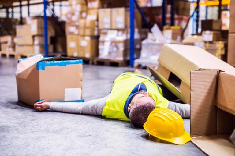 An accident in a warehouse. Man lying on the floor among boxes, unconscious