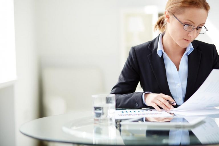 Young businesswoman sitting at workplace and reading paper in office