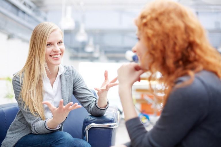 Portrait of young smiling businesswomen speaking to her colleague in office